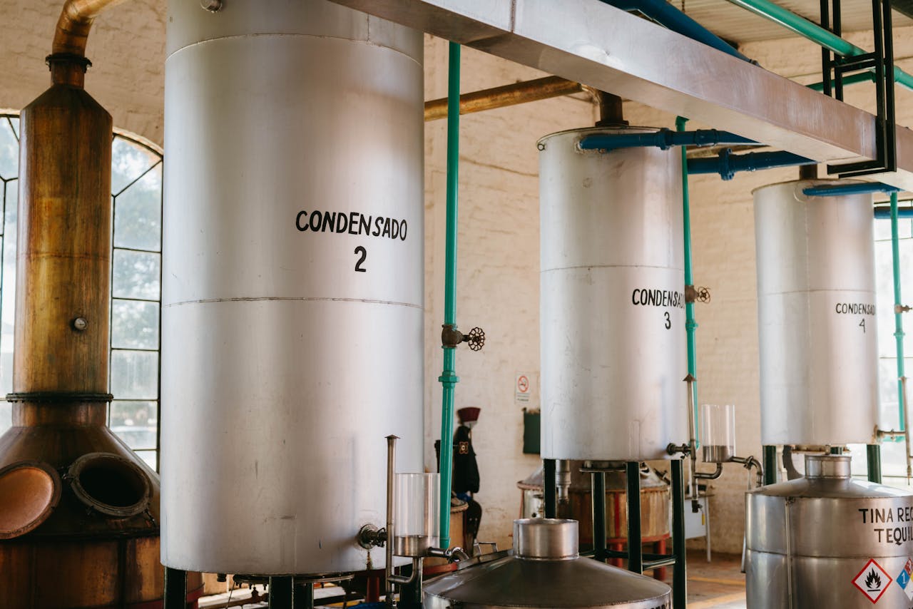Interior view of industrial tequila distillery with metal tanks and pipes.