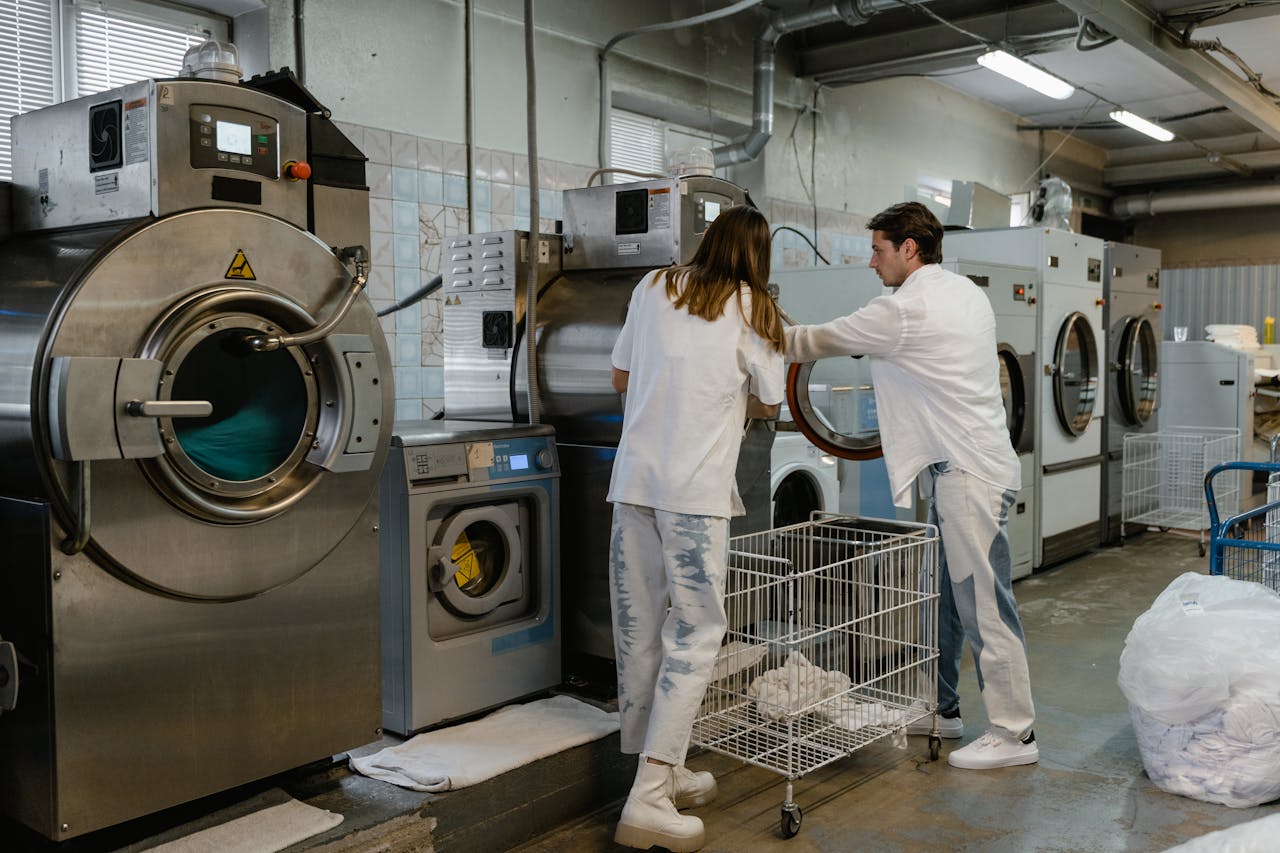 Two adults working in an industrial laundry facility with large machines.